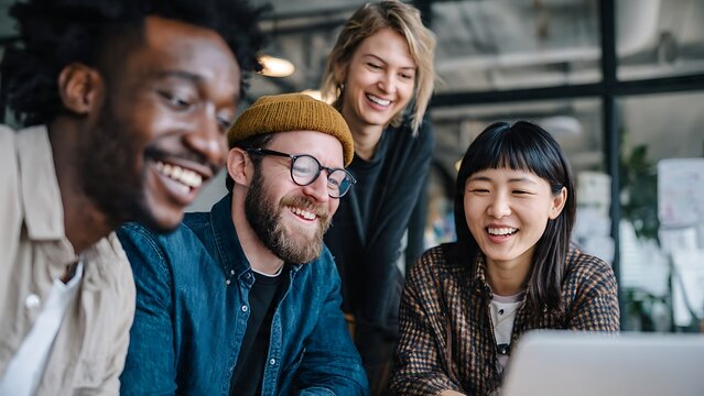 Group of cheerful diverse young creative professionals collaborating in a modern office, smiling while looking at a laptop screen together. Teamwork and startup success concept.