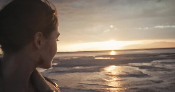 Cinematic silhouette of woman looking back over wet desert as sun sets - steady cam movement