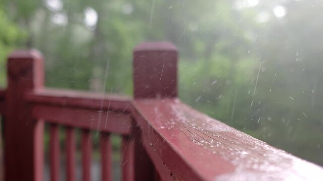 An atmospheric video of a rainstorm. Heavy rain and splashing. Large drops of downpour shatter against the wooden railing of a veranda or balcony. Slow motion.