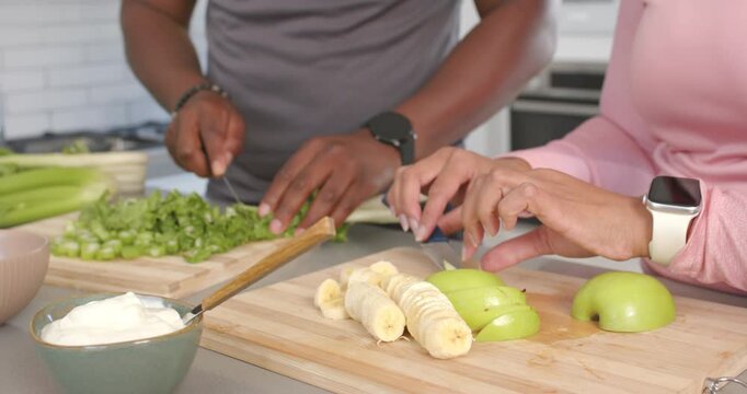 Prompted by fruits on board, African American couple chopping greens and slicing apples for snack