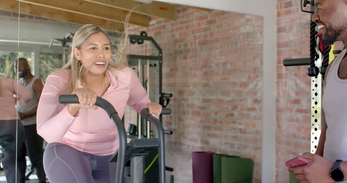 African American trainer tapping phone while guiding client using elliptical home gym high-fiving