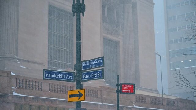 Vanderbilt Avenue street signs covered in New York snow. Snowy street signs for Vanderbilt Ave and East 43rd St with Grand Central Terminal blurred in background.