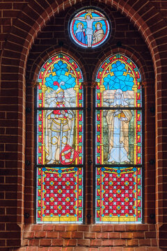Bad Doberan, Germany - 19 July 2025: View of Doberaner Munster featuring intricate stained glass windows depicting religious figures and a crucifixion scene set in red brick walls.