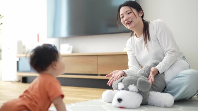 Mother smiles, teaching toddler with plush toy. Toddler crawls, curious and engaged. Playful interaction shows love and learning. Ideal for parenting, child development, or family content