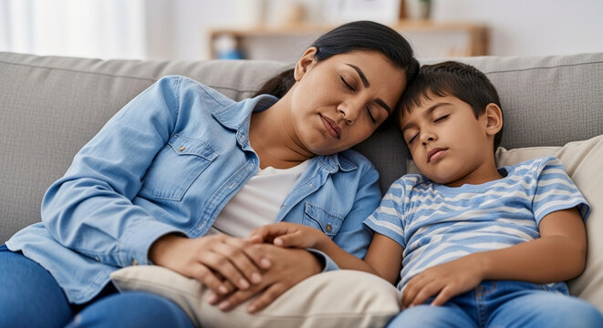 Peaceful Indian mother and son sleeping together on a grey couch in a living room, illustrating parental exhaustion, afternoon nap, and family love.