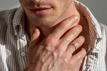 Fototapeta premium Man hand placed on collarbone sunlight grazing skin, close up of male chest and lips, textured stubble and ring