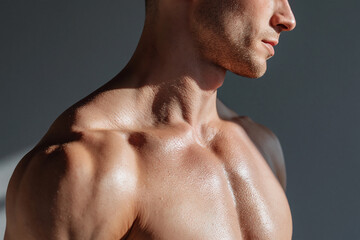 Naklejka premium Muscular male torso sunlit shoulder chest with sweat and stubble jawline in dramatic side lighting conveying strength and focus