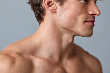 Naklejka premium Young male shoulder shifting away from light with highlight fading, close up profile of neck jawline and collarbone showing smooth skin and subtle stubble expressing calm confidence