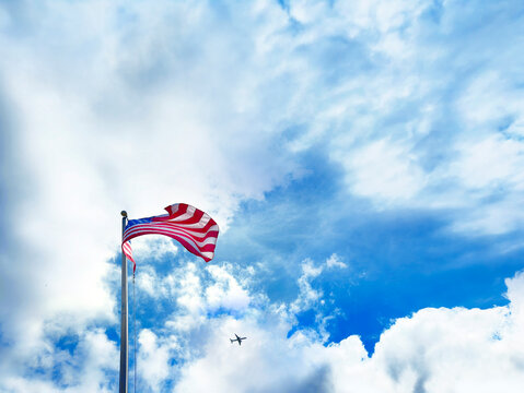 American Flag and flying airplane over cloudy sky