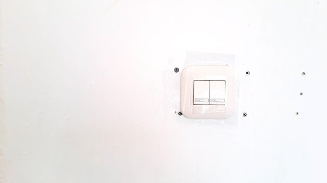 Close up of an Asian man hand turning on a white wall light switch in a minimalist workspace. Young male finger pressing the button to switch on the lights, initiating work or saving energy concept. 