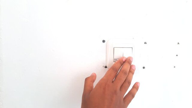 Close up of an Asian man hand turning on a white wall light switch in a minimalist workspace. Young male finger pressing the button to switch on the lights, initiating work or saving energy concept. 