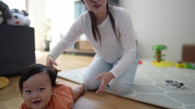 Mother smiles warmly while baby crawls on floor. Soft light bathes wooden floor, cozy home setting. Child explores world with curious hands and eyes. Perfect for parenting, child development