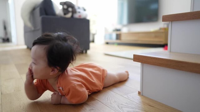 Baby crawls on wooden floor near staircase steps. Child's eyes look curious, curious, focused ahead. Home's warm lighting highlights baby's soft skin. Perfect for parenting, baby development