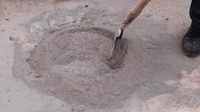Worker repairing pothole on damaged road with shovel