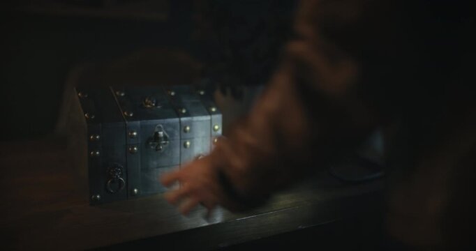 Woman slowly unlocking mysterious small chest on desk in spooky room at night