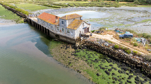 Alhos Vedros, Portugal - 16 December 2024: Aerial view of the historic tide mill with orange-tiled roofs situated on the edge of a marshy estuary with stone walls and mudflats.