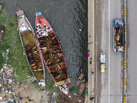 Dhaka, Bangladesh - 25 May 2026: Aerial view of cattle being transported on traditional wooden boats along the Buriganga River next to a busy bridge with a truck.