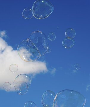 Soap bubbles float in front of a clear blue sky with a small white cloud, Spain