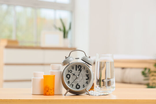 Alarm clock with pill bottles and glass of water on table in bedroom