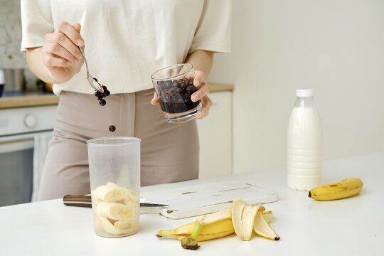 Unrecognizable woman puts blackcurrants in a blender to mix them with a chopped banana