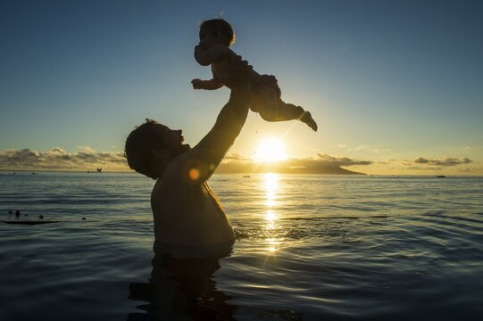 Father playing with his little baby in the water at sunset, Papeete, Tahiti