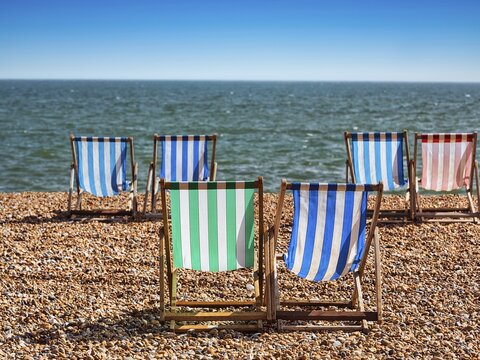 Colourful deckchairs by the sea, paired folding chairs on a shingle beach, Brighton, England, United Kingdom