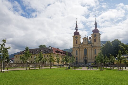 Baroque church with red roofs, surrounded by trees and green meadow with cloudy sky, monastery and pilgrimage church of the Visitation of Mary, Hejnice, Haindorf, Liberec, Czech Republic