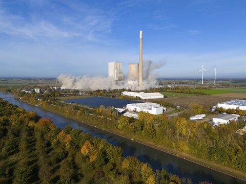 A coal-fired power station with smoking chimneys in a rural setting, surrounded by wind turbines and a canal, blasting of the ash silos, coal-fired power station, Mehrum, Peine district, Mittellandkanal, Lower Saxony, Germany