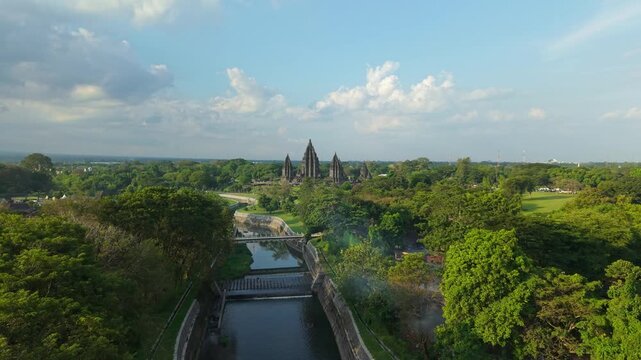 Aerial view of the ancient Prambanan Temple complex surrounded by dense green trees and a winding river under a cloudy sky Kecamatan Prambanan, Daerah Istimewa Yogya, Indonesia.