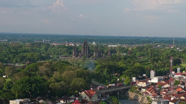 Aerial view of Prambanan Temple rising above lush green trees and urban rooftops in Kecamatan Prambanan, Daerah Istimewa Yogya, Indonesia.