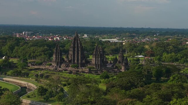 Aerial view of the ancient Prambanan Temple complex with its towering stone spires surrounded by lush green trees in Kecamatan Prambanan, Daerah Istimewa Yogya, Indonesia.