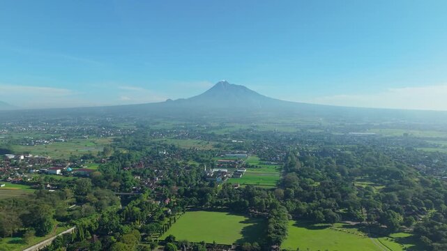 Aerial view of the majestic Mount Merapi volcano towering over the lush green plains and rural settlements near Kecamatan Prambanan, Daerah Istimewa Yogya, Indonesia.