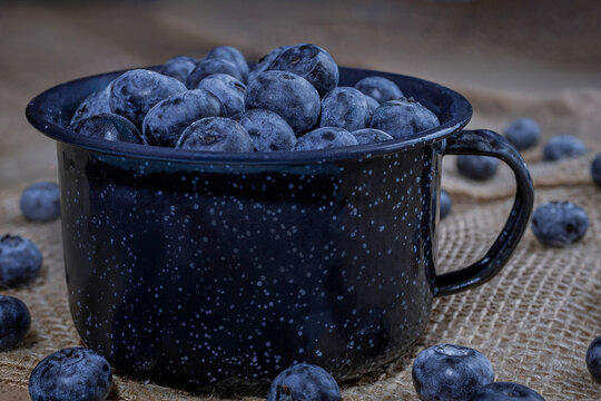 Fresh Ripe Blueberries in Dark Vintage Enamel Mug on Burlap