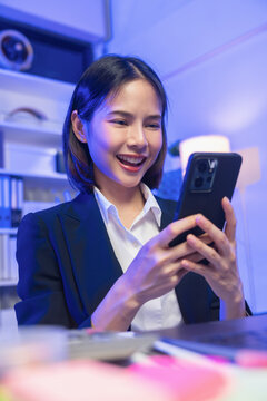 Smiling young Asian businesswoman using smartphone while wearing headset in office.