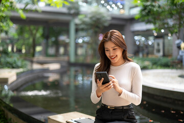 Fototapeta premium Asian woman smiling using smartphone outdoors in city