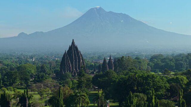Aerial view of the ancient Prambanan Temple complex with the smoking Mount Merapi volcano in the background in Kecamatan Prambanan, Daerah Istimewa Yogya, Indonesia.