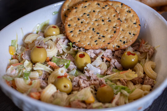 Ensalada de atun con lechuga mayonesa y aceitunas rellenas, con galletas de ajonjoli encima dentro de un tazon blanco, vista con angulo, imagen de acercamiento