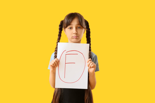 Sad schoolgirl holding paper with bad grade on yellow background