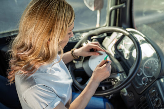 Closeup shot, woman trucker filling up tachograph chart disc by hand on the steering wheel 