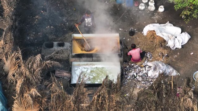 Natore, Bangladesh - 13 March 2024: Aerial view of workers boiling date palm juice in large pans to produce traditional jaggery with steam rising in a rural setting.