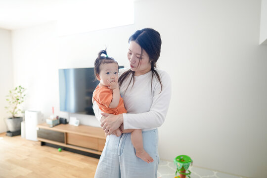 Soft light fills a minimalist living room. Mother holds her baby close, eyes full of tenderness. The child gazes curiously, tiny fingers near their mouth