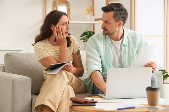 Young couple using laptop to pay bills at home. Bankruptcy concept