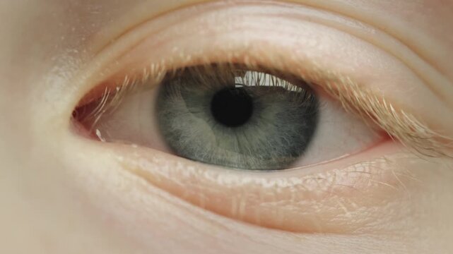 A detailed close up of a baby's eye opening and closing slowly, revealing light blue iris and tiny pupil, extreme macro dynamic shot of a child's face.