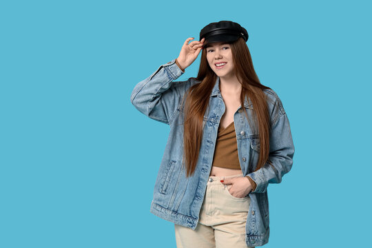 Stylish young girl in hat and jeans jacket on blue background