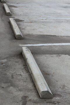 Concrete parking stops line a weathered asphalt lot with white painted markers