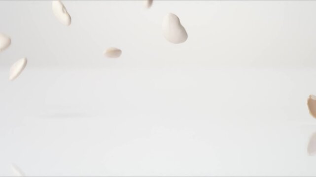 Dried raw Lima Beans bouncing on a white tabletop in slow motion close up macro before settling.