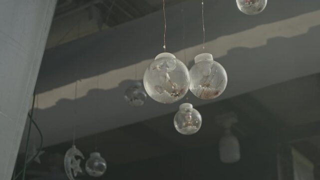 A static shot of glowing glass spheres filled with white particles and moon-shaped decorations hanging from copper strings in a dimly lit, atmospheric space.