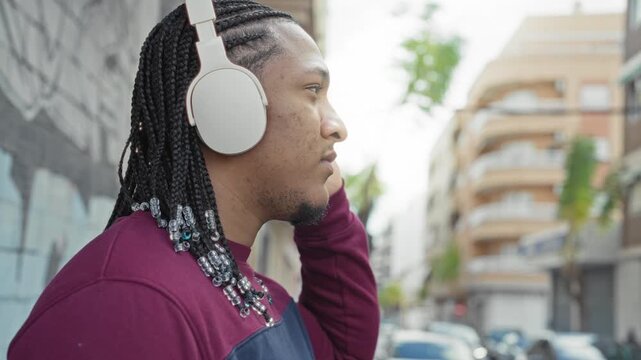 Man wearing white headphones touches earpiece on a street while listening to music; calm focus solitude.