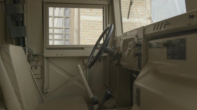 A detailed 4K interior shot of a military utility vehicle, highlighting the steering wheel, minimalist dashboard, and functional cockpit design typical of tactical transport.