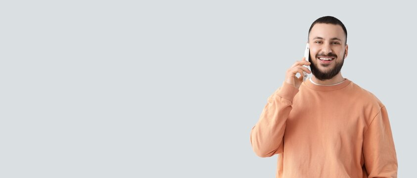 Young man talking by mobile phone on light background with space for text